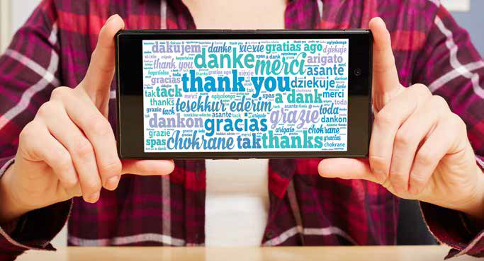 Eine Person im karierten Hemd hält ein Tablet hoch, auf dem der Satz „Danke“ in verschiedenen Sprachen wie Englisch, Spanisch und Deutsch steht. Diese bunte Wortwolke betont virtuelle Zusammenarbeit und globale Dankbarkeit.
