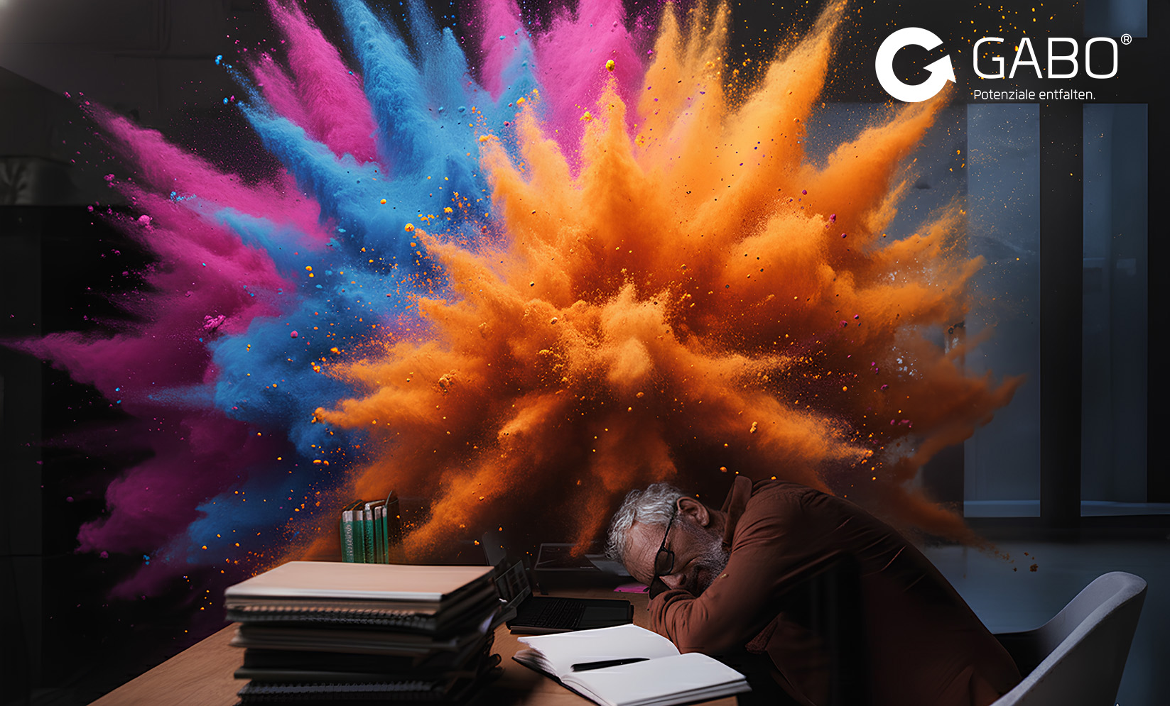 Ein Mann schläft an einem mit Büchern und Ordnern bedeckten Schreibtisch, während hinter ihm ein dramatischer Ausbruch von buntem Pulver explodiert. Das GABO-Logo und der Slogan sind in der oberen rechten Ecke zu sehen.
