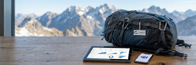 Ein schwarzer Rucksack, ein Tablet mit Diagrammen und ein Smartphone liegen auf einem Holztisch, während im Hintergrund durch ein großes Fenster schneebedeckte Berge zu sehen sind.